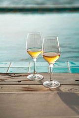 Two glasses of wine  on the edge of infinity swimming pool with panoramic views of the sea at sunset. Drink, celebrate, vacation and summer concept.