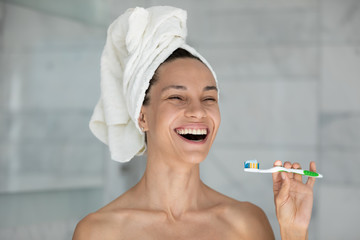 Head shot woman after morning shower wears towel on head holds toothbrush laughing having wide toothy smile perfect straight white teeth, oral hygiene treatment and products for healthy tooth concept