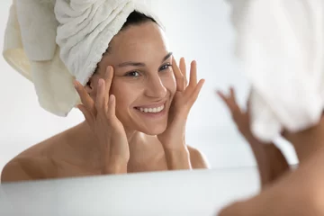 Poster Nach dem Beauty-Home-Spa-Verfahren sieht sich die Frau die perfekte Haut im Spiegel-Touch-Gesicht an und fühlt sich zufrieden. Reinigende Gesichtsmaske, Anti-Falten-Creme, chemisches Peeling, Anti-Aging-Behandlung im Klinikkonzept © fizkes