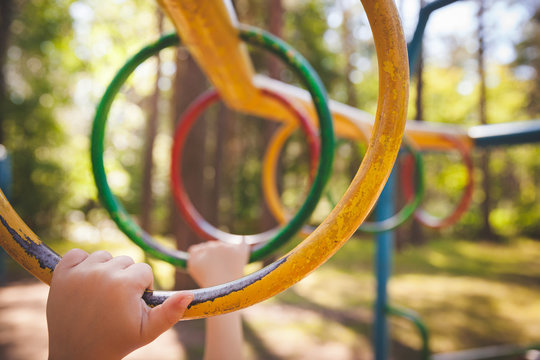 Hands Of A Little Boy Hold On To The Crossbar At The Playground. The Kid Is Climbing The Monkey Bar In The Playground. Early Development And Healthy Lifestyle