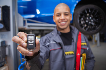 Cheerful car service worker holding out car key to the camera after repairing automobile successfully