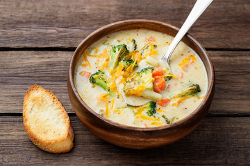 Wooden bowl of creamy broccoli cheddar cheese soup with toasted  bread