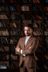 portrait of a young bearded businessman in a brown suit against the background of the library