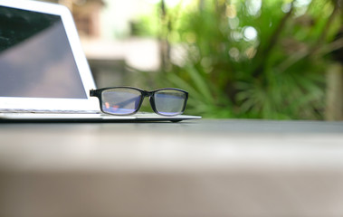 Spectacles on top of computer laptop with home and green nature background. Copy space.