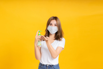 Young asian woman with medical mask protection coronavirus COVID-19 applying alcohol gel clean hands healthy and safety care concept on yellow background isolated studio shot, copy space.