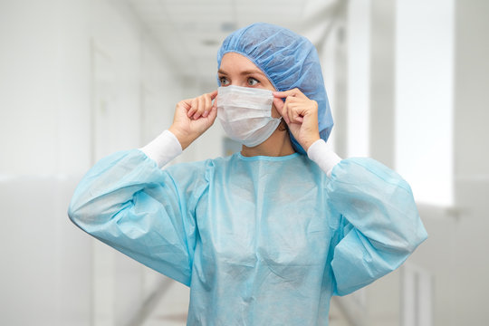 Portrait Of Doctor In Scrubs. A Female Doctor In A Protective Cap And Face Mask In Safety Measures Against The Coronavirus.