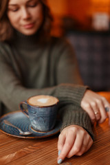 Fototapeta na wymiar young and beautiful girl in a green sweater sits with a cup of coffee
