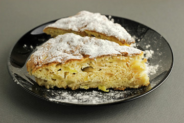 Delicious apple pie, charlotte is sprinkled with powdered sugar on a black plate on a dark background. Close up side view.
