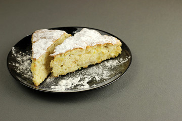Delicious apple pie, charlotte is sprinkled with powdered sugar on a black plate on a dark background. Close up side view.