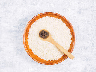 Indian long grain Basmati rice in brown wooden bowl and allspice in spoon on white concrete background