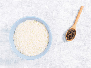 Indian long grain Basmati rice in blue ceramic bowl and allspice in spoon on white concrete background