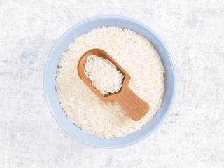 Indian long grain Basmati rice in blue ceramic bowl and wooden scoop on white concrete background