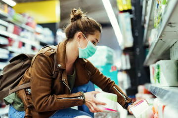 Young woman wearing face mask while buying toilet paper in the store.