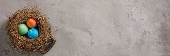 Easter eggs in a bird's nest on a textural background. Easter celebration concept. Copy space. Flat lay. Banner.