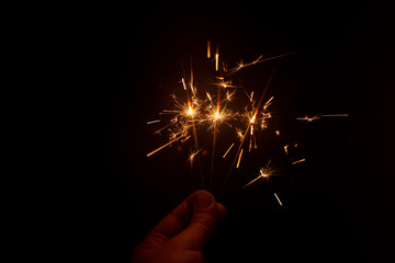 Fingers holding up bright sparked fireworks in dark