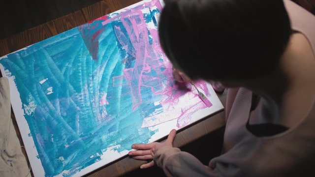 Painting hobby. Recreative leisure. Enthusiastic female artist making lines on canvas with spatula.