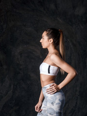 Fototapeta premium Portrait of young beautiful sportive girl posing over dark background.