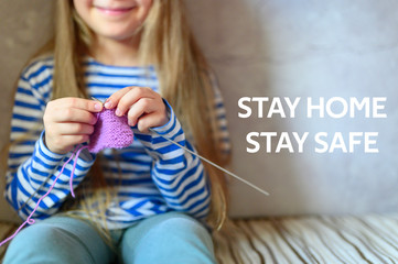 kid girl knitting with needles. the concept of teaching and studies at home during the quarantine. text stay home stay safe ofl font