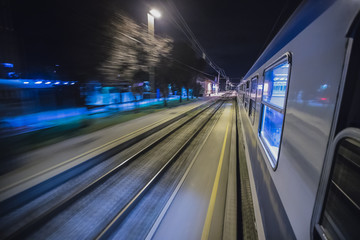 Traveling with a train, looking out of the window at night. Motion blur of tracks next to a train while moving through the station.