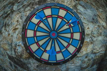 Closeup fisheye photo of round dartboard in black, red, blue and white hanging on a vintage stone wall outside. Garden or porch entertainment.