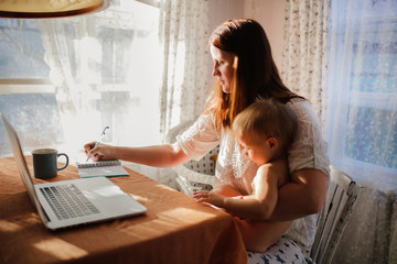Caucasian mom works on laptop with baby on hands