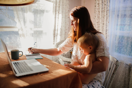 Caucasian Mom Works On Laptop With Baby On Hands