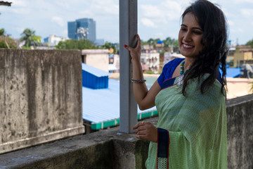 Portrait of a beautiful smiling brunette Indian Bengali woman in traditional wear sari standing on...