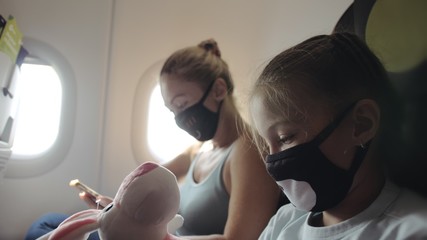 Family woman and child baby travel tourist caucasian at plane aircraft with wearing protective medical mask. Use smartphone mobile. Health virus protect coronavirus epidemic sars-cov-2 covid-19.