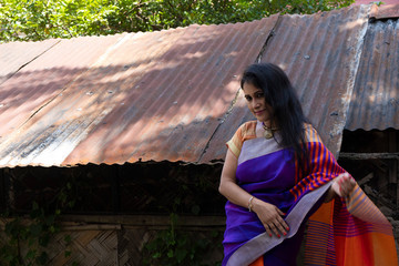 Portrait of a beautiful brunette Indian bengali thoughtful woman in traditional wear sari standing...