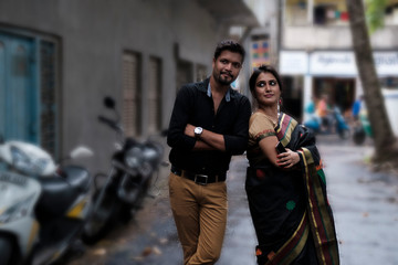 A brunette Indian Bengali romantic couple in traditional wear interacting between themselves in the drenched street in the morning of Durga Puja festival in urban background. Indian lifestyle.