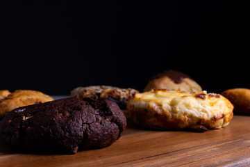 Different cookie cakes laying on a wooden board in front of a black background