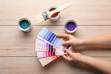 Female hands with color swatches and paint on wooden table