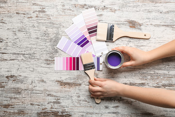 Female hands with color swatches, brushes and paint on wooden table