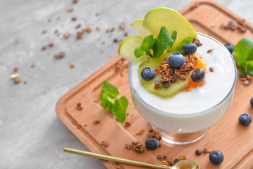 Glass with tasty yogurt, granola and fruits on table