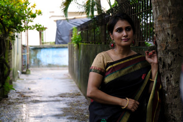 Portrait of a beautiful brunette Indian bengali thoughtful woman in traditional wear sari standing...