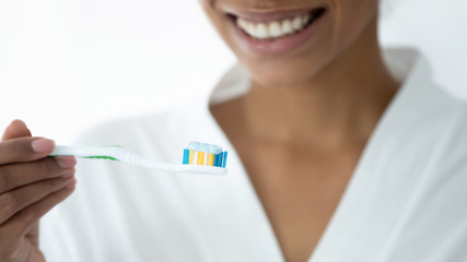 Close up African woman holding toothbrush with toothpaste, on background charming perfect smile of...