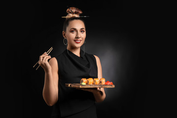 Fototapeta premium Smiling woman holding a wooden board with fresh salmon sushi rolls, wasabi, and pickled ginger
