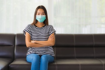 Portrait beautiful young asian woman with mask on sofa in living room for protect coronavirus or...