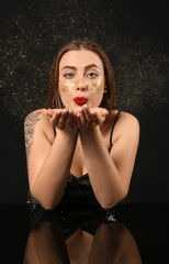 Fashionable young woman with glitters on her body against dark background