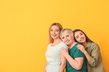 Portrait of mature woman with her adult daughter and mother on color background