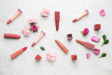 Different lipsticks and flowers on light background