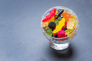 Colored candies inside a glass cup on dark background. Top view with space for your greetings