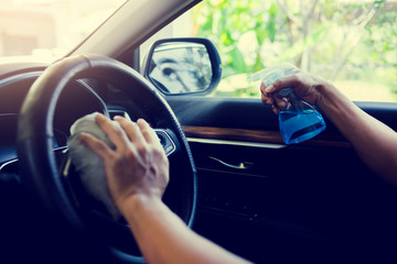 Hand of driver is spraying alcohol to car steering wheel to kill the Coronavirus Covid19 or contamination of germ. Driver is cleaning and wipe surfaces that are frequently touch with spraying alcohol.