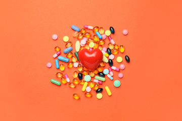 Red heart and pills on color background. Cardiology concept