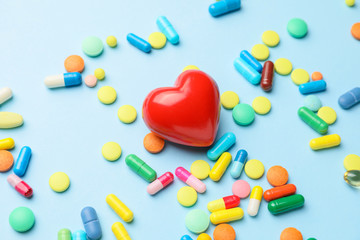 Red heart and pills on color background. Cardiology concept