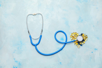 Heart made of pills and stethoscope on color background