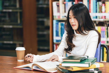 Young beautiful asian student girl working a book, learning in college library in university