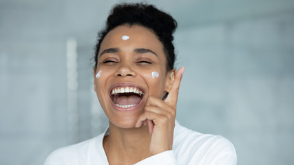 Cheerful lively african woman wear white bathrobe singing during morning routine skincare home spa...
