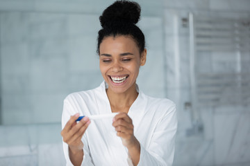 Beautiful african young woman apply pregnancy test see two stripes results feels happy by long awaited planned gestation. Modern rapid accurate test, first time pregnant female enjoy moment concept