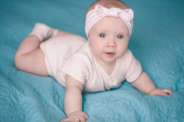 Newborn girl with a headband is lying on a blue blanket